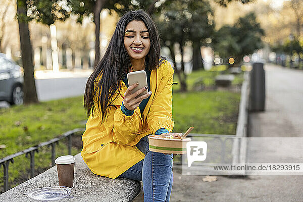 Happy young woman using smart phone on seat