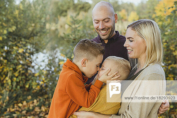 Happy parents looking at son rubbing nose with brother in autumn