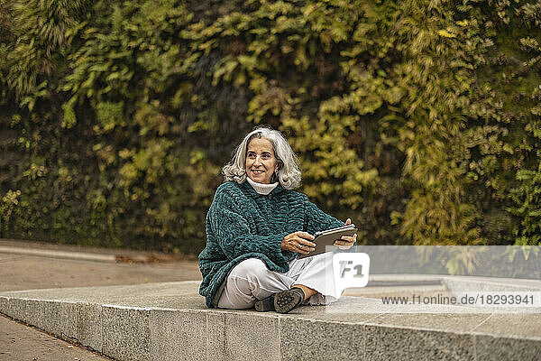 Glückliche ältere Frau sitzt mit Tablet-PC vor Pflanzen