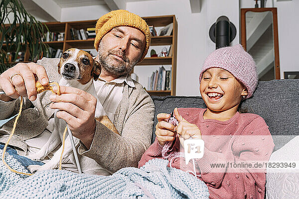 Father and happy daughter with dog knitting on couch at home together