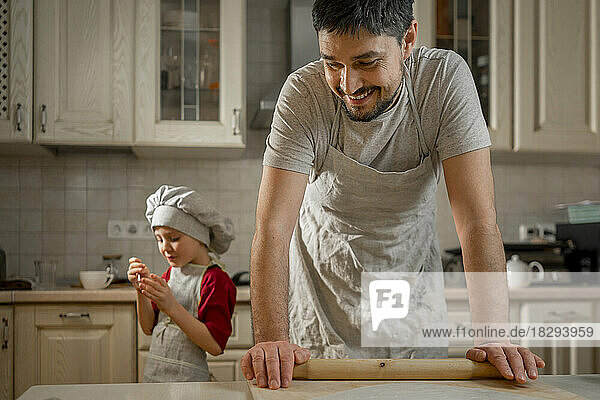 Smiling father with rolling pin by son in kitchen at home