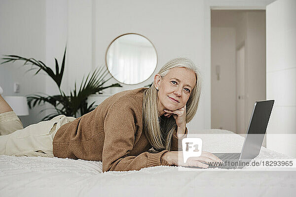 Mature woman lying with hand on chin in bedroom