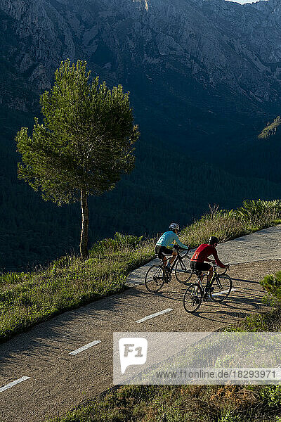 Mature cyclists riding bicycles on road in front of mountain