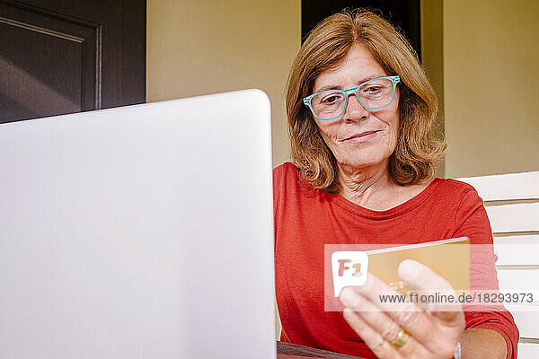 Senior woman holding credit card doing online shopping at front porch