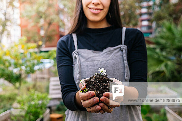 Smiling woman holding dirt with small flower in cupped hands