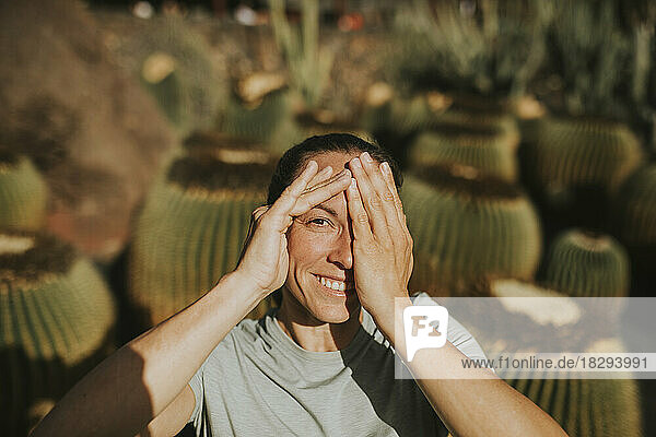 Lächelnde Frau  die an einem sonnigen Tag das Auge mit der Hand bedeckt