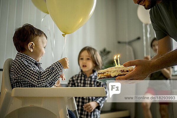 Father holding cake and celebrating son's birthday at home