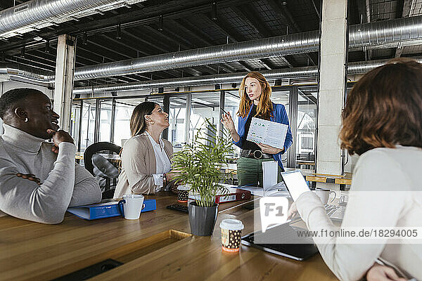 Redhead businesswoman discussing over document with colleagues in coworking office