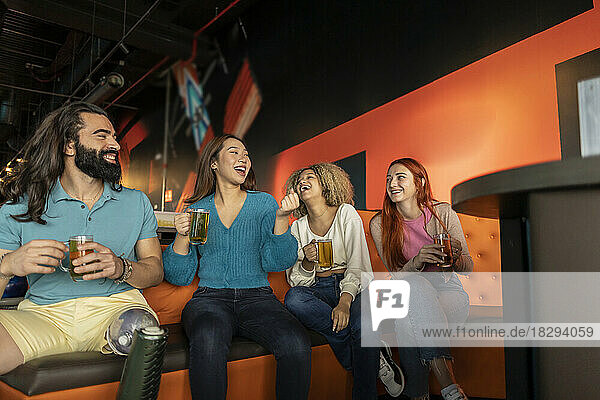 Multiracial friends drinking beer on sofa at bowling alley