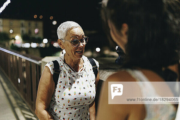 Senior woman talking with young friend on bridge at night