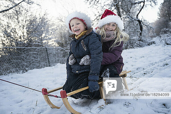 Happy brother and sister sitting on sled in snow