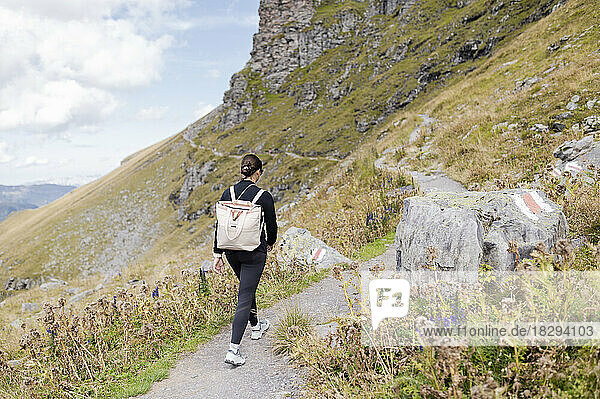 Young hiker with backpack walking on footpath at mountain
