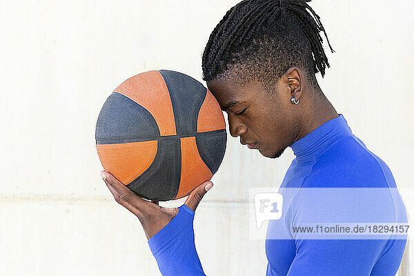 Young man holding basketball in front of wall