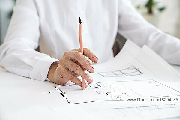 Engineer holding pen with blueprint on table in office