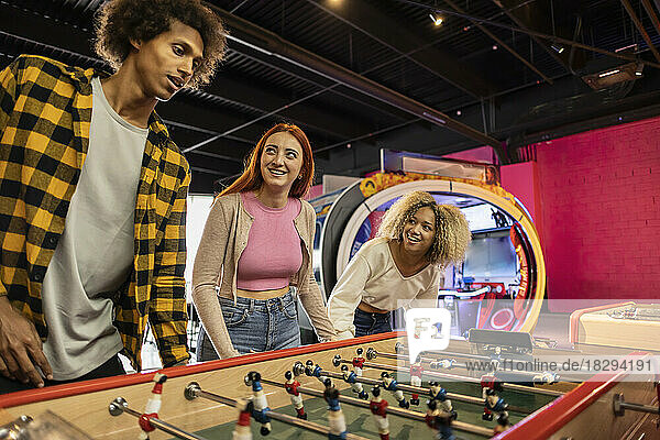 Happy young friends playing foosball at arcade