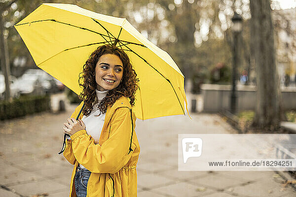 Happy beautiful woman with yellow umbrella standing at footpath