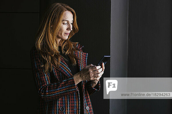 Redhead businesswoman using smart phone in front of black wall
