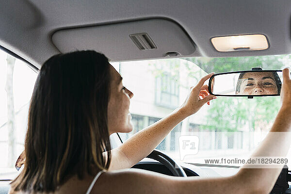 Young woman adjusting rear view mirror in car