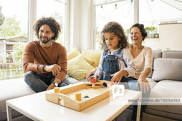 Happy man and woman with daughter playing board game in living room at home
