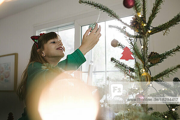 Lächelndes Mädchen mit einer Kugel  die zu Hause am Weihnachtsbaum hängt