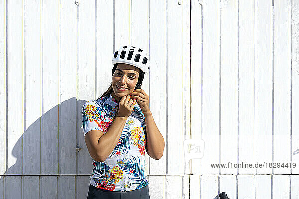 Happy cyclist adjusting helmet in front of white wall
