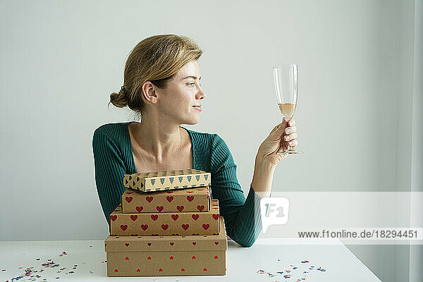 Smiling woman looking at glass of champagne sitting on table with stack of gifts
