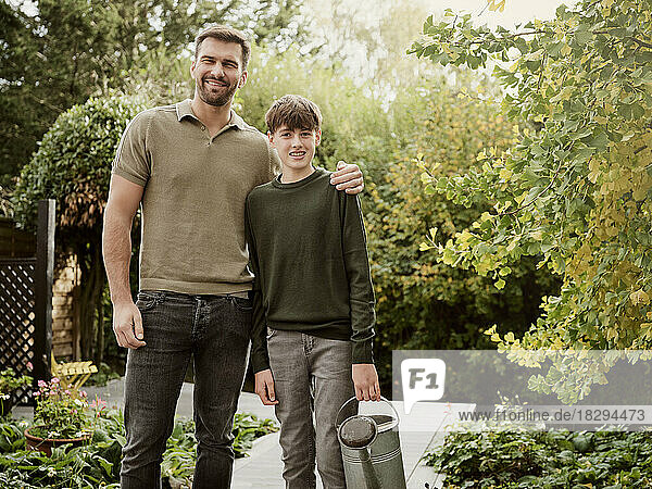 Father and son standing in garden boy carrying watering can after gardening