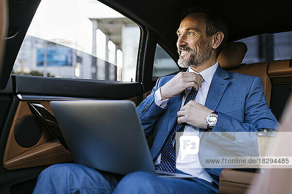 Smiling businessman adjusting necktie in car