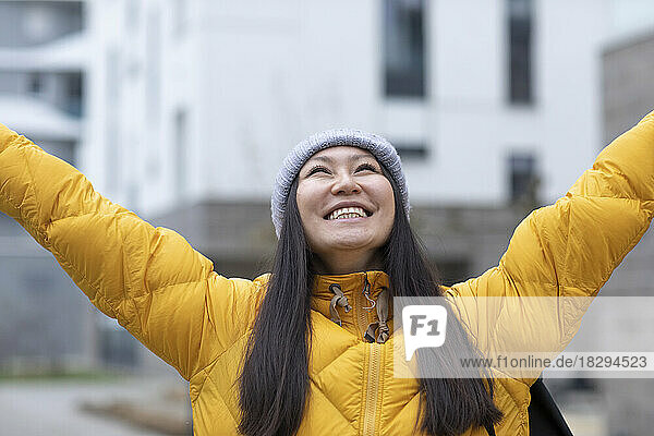 Happy woman wearing knit hat standing with arms raised