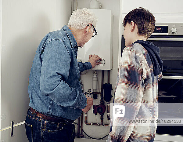 Grandson and grandfather adjusting boiler for energy saving at home