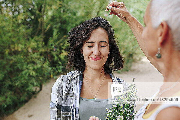 Senior woman putting flowers on friend's hair at park