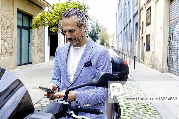 Mature businessman using mobile phone sitting on motorcycle