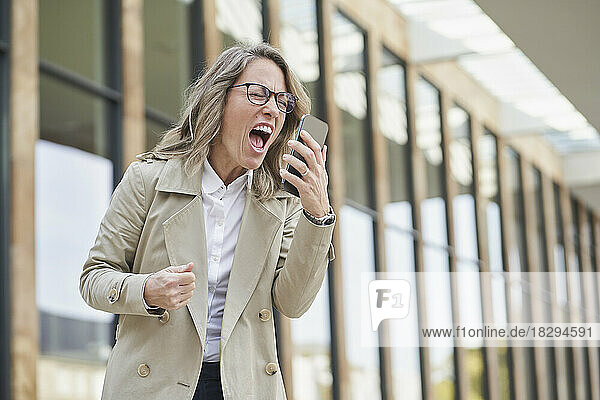 Mature businesswoman shouting on speaker phone outside building