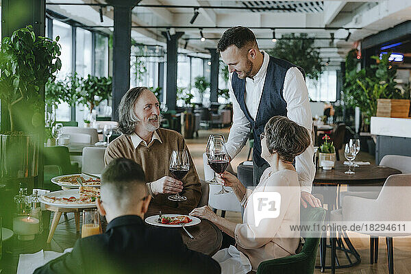 Mann prostet Weinglas mit Familie im Café an