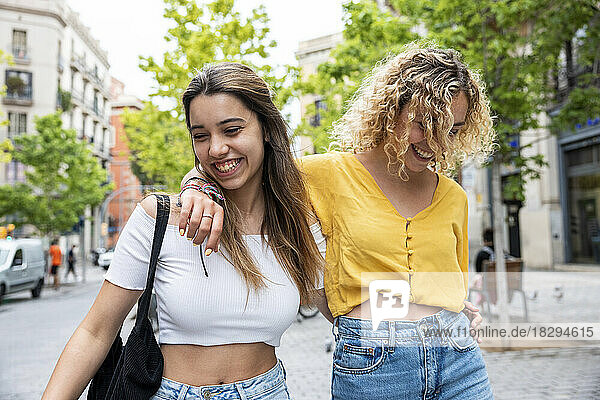 Happy young woman with friend walking on footpath