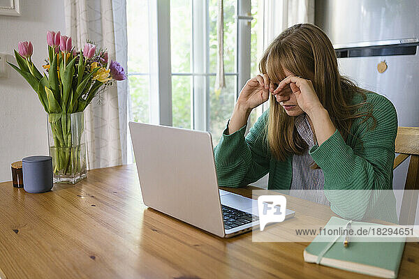 Tired freelancer rubbing eyes sitting with laptop at table