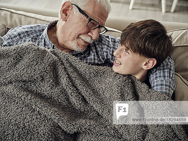 Grandfather and son snuggling under a blanket on couch in living room