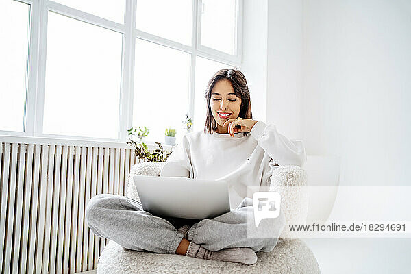 Happy woman using laptop sitting cross-legged at home