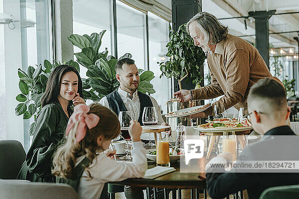 Älterer Mann serviert Familie im Café Essen