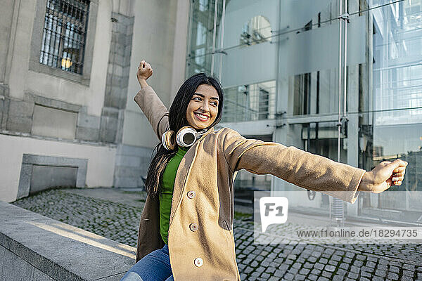 Happy young woman stretching arms outside building