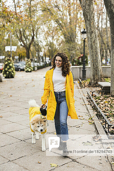 Smiling young woman walking with dog on footpath