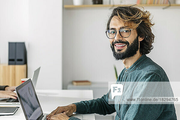 Happy freelancer with laptop at desk in office