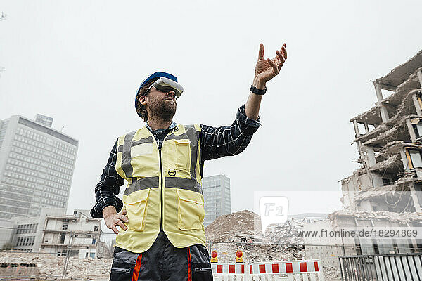 Worker wearing virtual reality glasses gesturing in front of construction site
