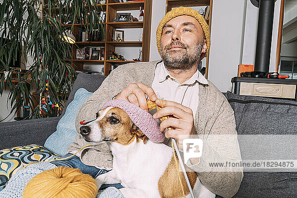 Mann mit Hund strickt zu Hause auf der Couch