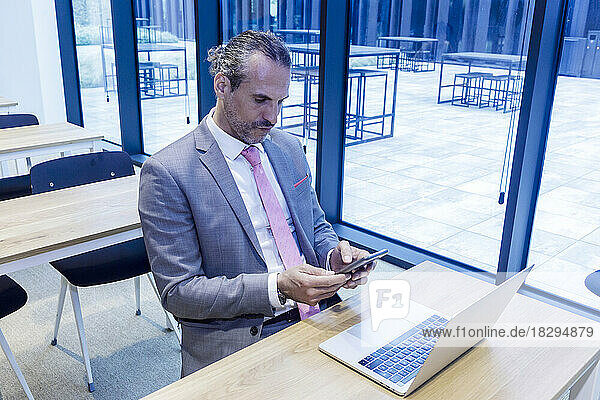 Mature businessman using smart phone by laptop at desk in office