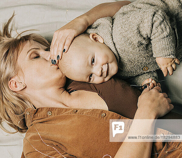 Mother kissing baby boy lying on bed at home