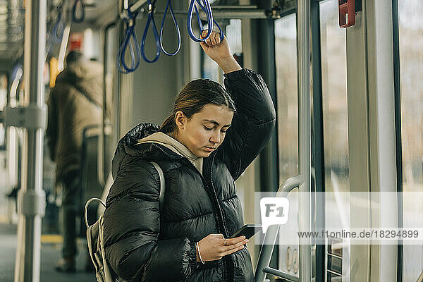 Teenage girl using smart phone standing in tram