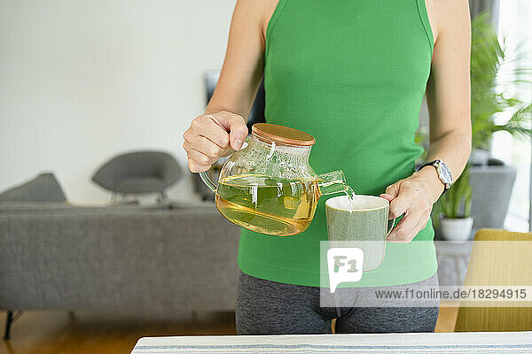 Frau gießt zu Hause Tee in eine Tasse