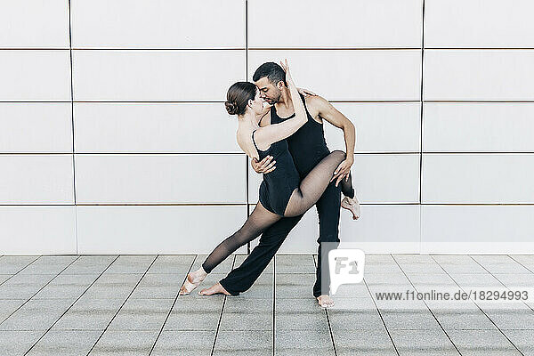 Couple performing ballet dance in front of wall