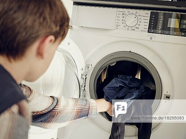 Boy putting laundry into washing machine at home